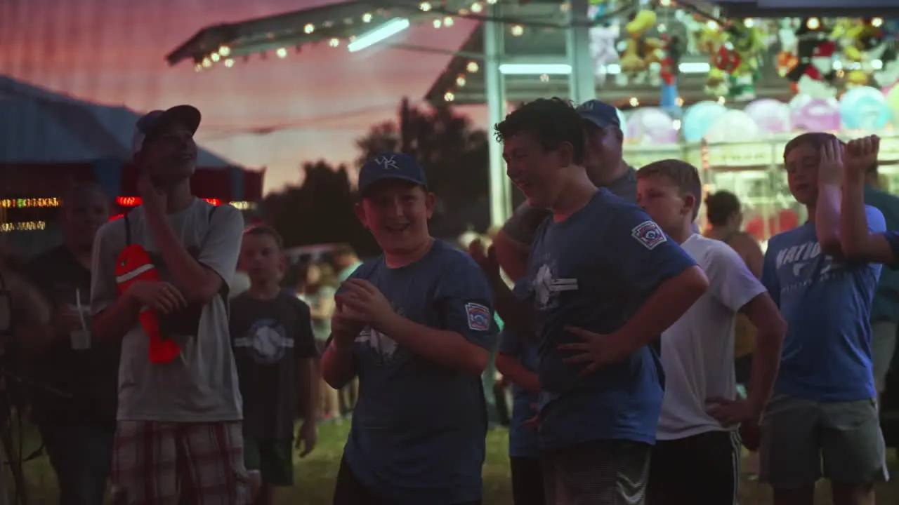 Young boy with friends playing speed pitch game at carnival at dusk