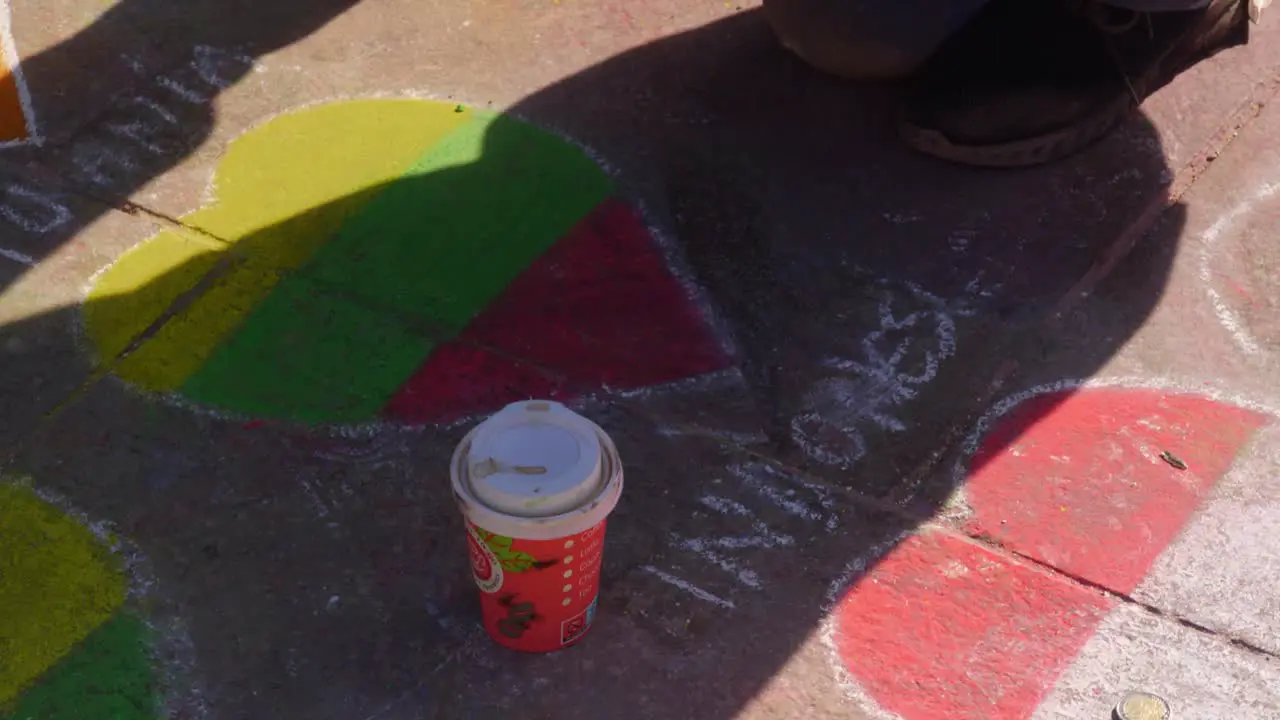 Medium shot of a person drawing hearts with chalk on the the sidewalk with a cup of coffee sitting on the ground shadow handheld