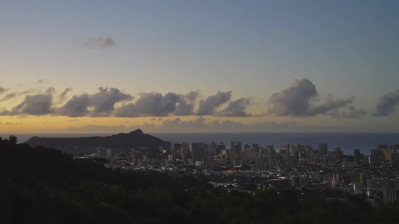 an orange sky looms over Honolulu Hawaii just after sunset as a view from a mountain with a white puffy cloud shelf