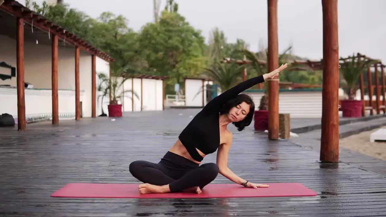 Brunette Woman Is Doing Yoga On Mat Outdoors The Girl Performs Yoga From The Sit Pose Bending Torso On Sides