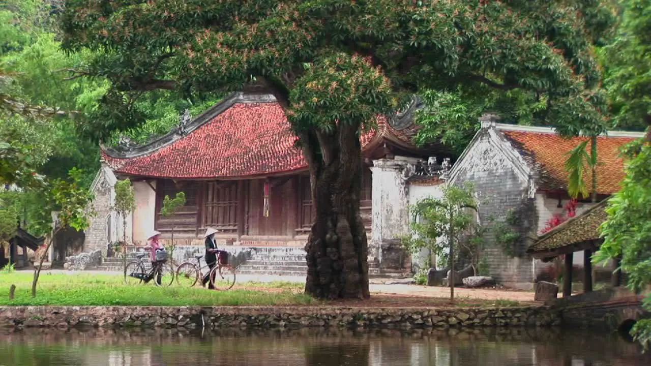 People walk their bicycles past a temple in Vietnam