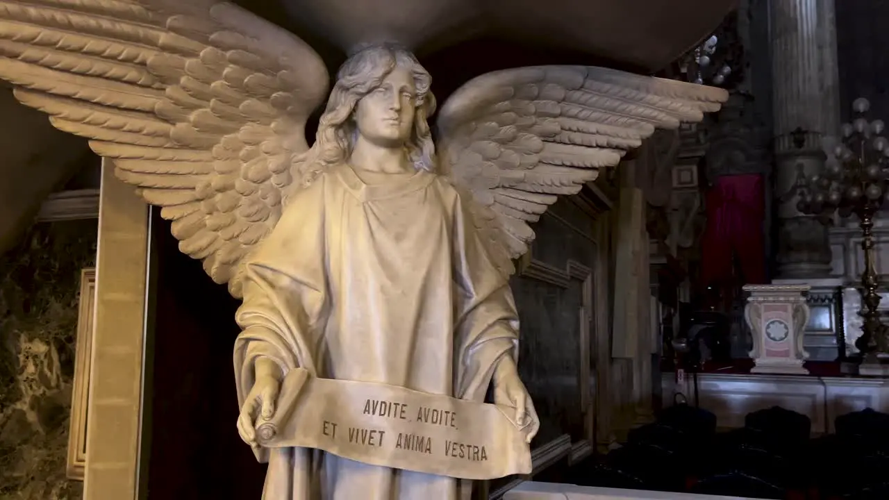 Slow pan around life size marble statue of an angel in Candelária church with a text written in Latin on a banner in hands in front of the altar