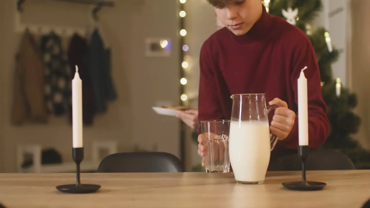 A Blond Boy And His Blond Sister Place An Empty Glass A Jug Of Milk And A Plate Full Of Cookies On An Empty Table With Two Candles Then They Leave The Room