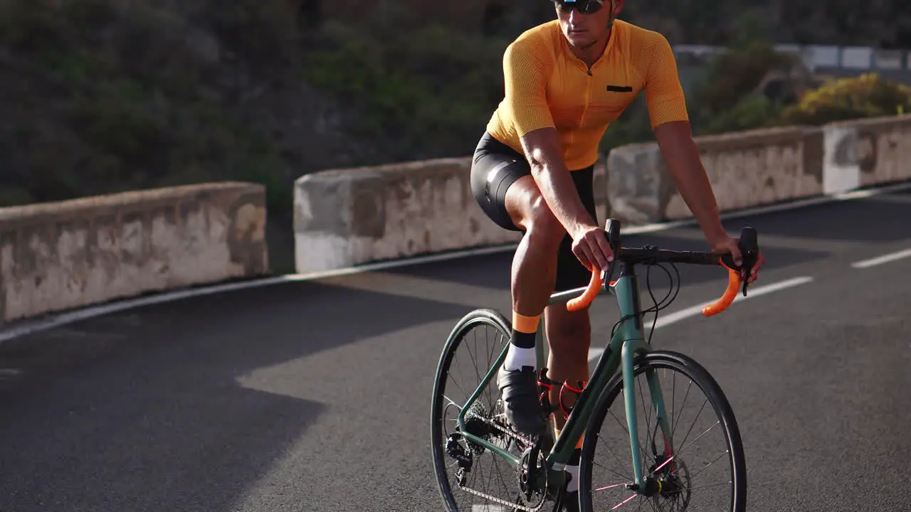 A man in a yellow t-shirt and helmet seated on a bicycle gazes into the distance while positioned on a mountain road