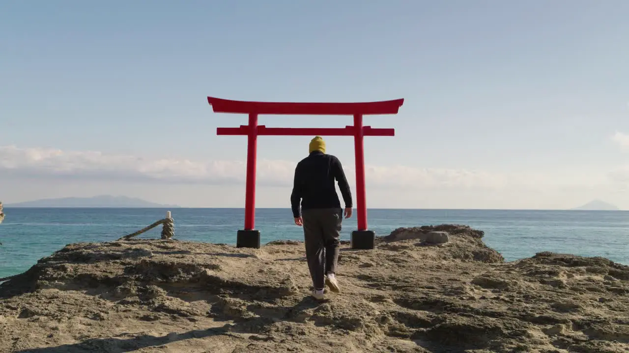 Young male walking toward Japanese red torii gate in front of ocean