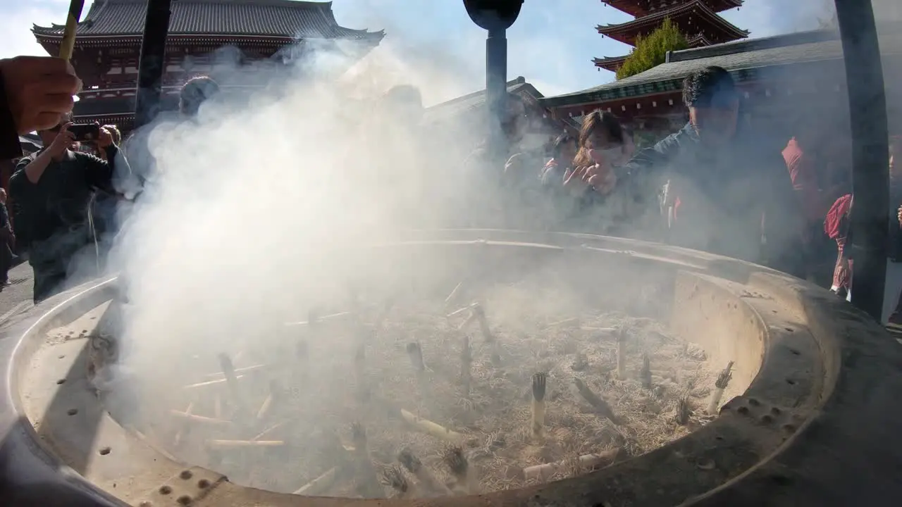 People waving in the smoke of an Incense Burner At A Temple In Tokyo Japan