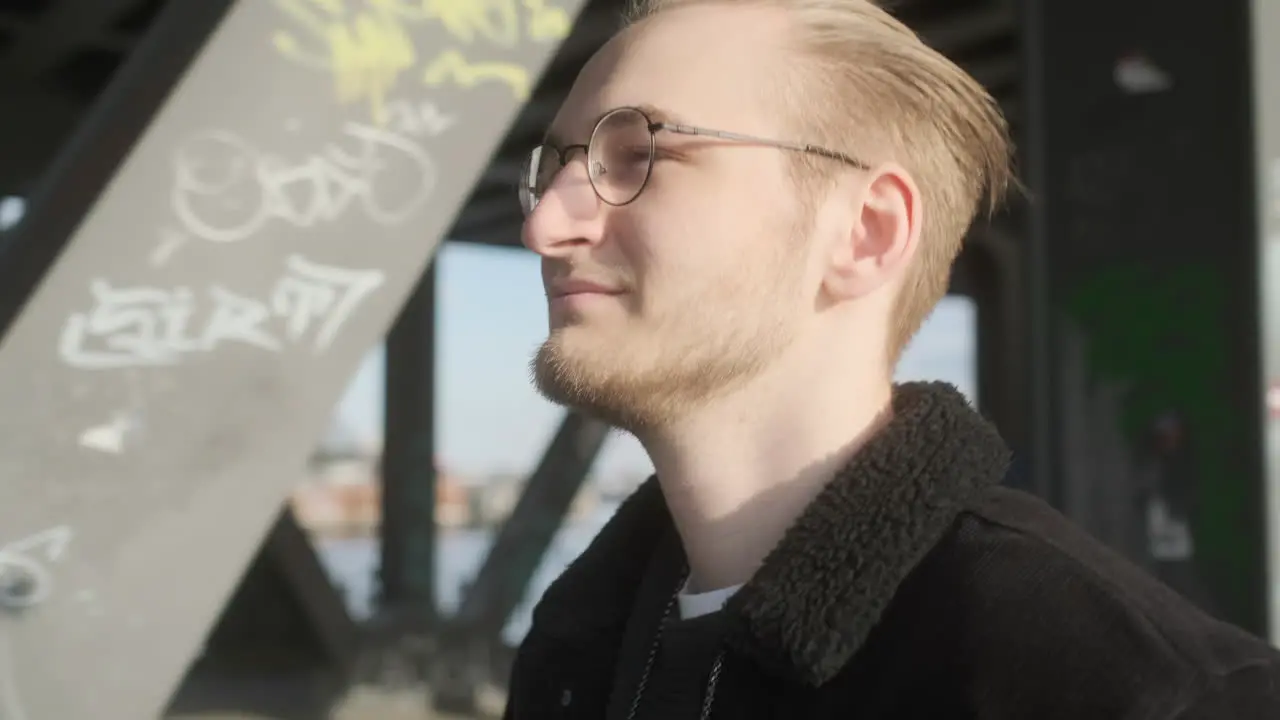 Young European Man with Glasses Beard and Man Bun Walking on Sidewalk on a Sunny Evening in Hamburg Germany