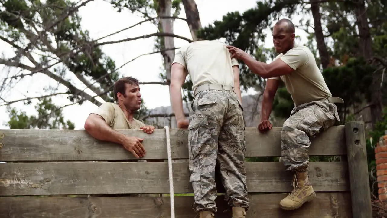 Male soldiers assisting their team mate to climb a wooden wall 4k