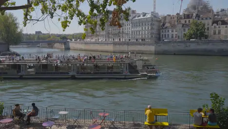 Tourist Boat In Quais De Seine Area Of Paris France With People On Banks Of River