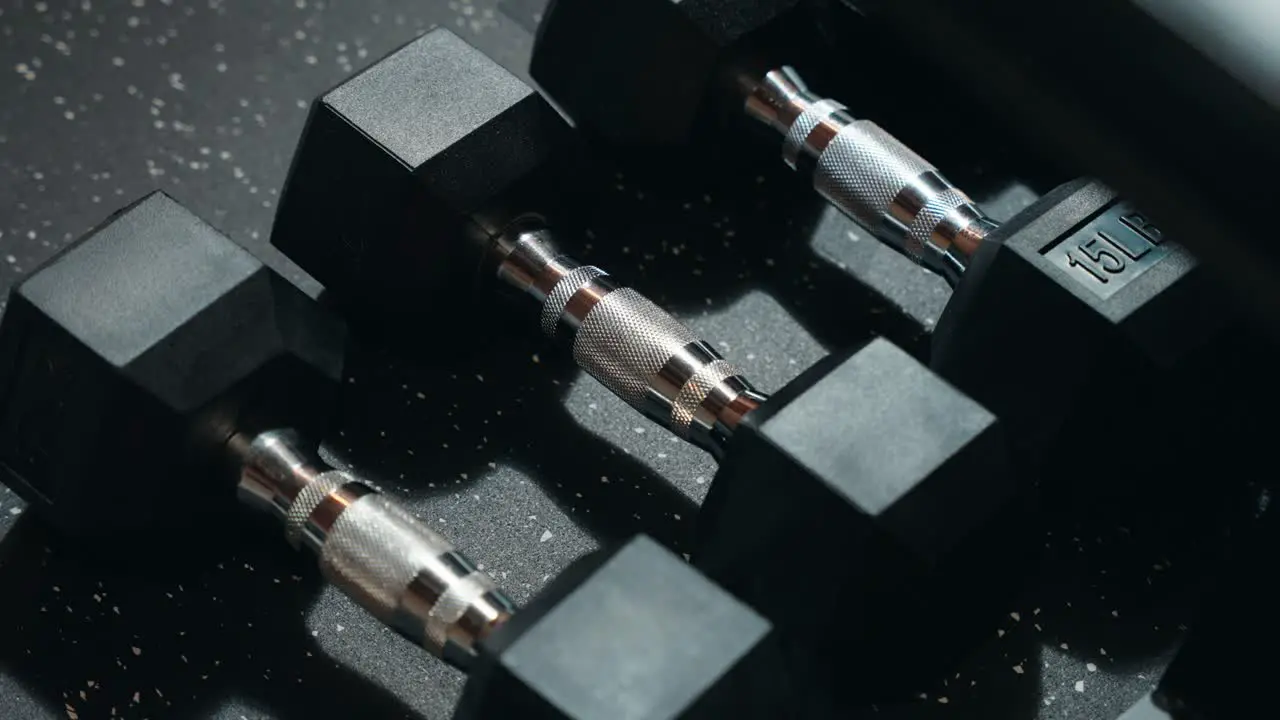 A 4K Row of Basic Black and Knurled Silver Metal and Rubber Weighted Exercise Dumbbells on a Synthetic Gym Mat Inside a Workout Center