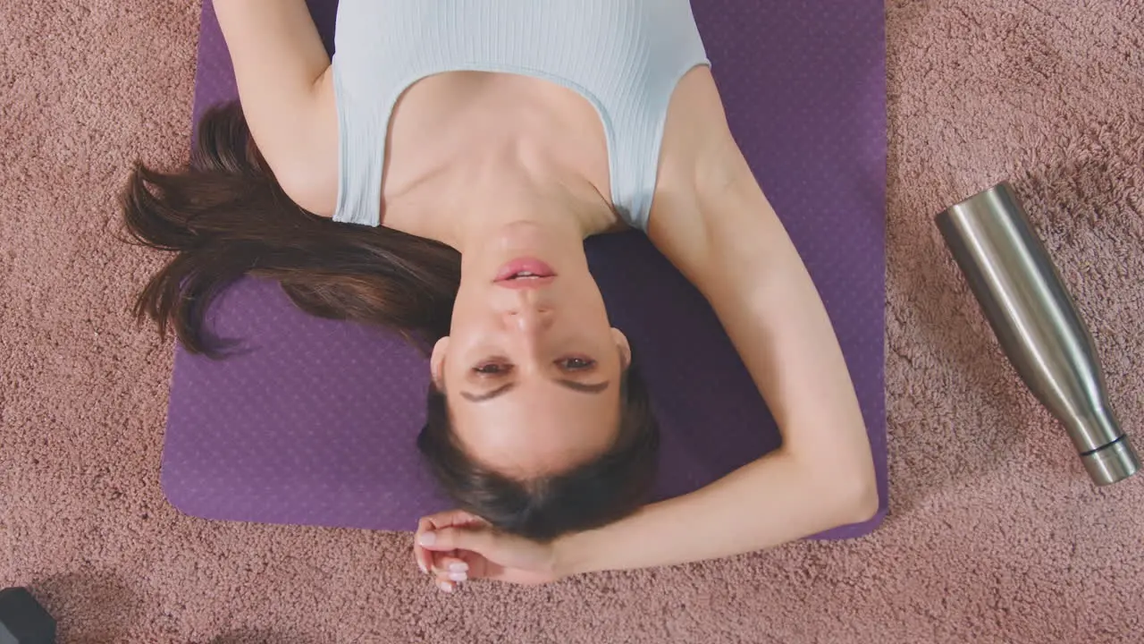 Overhead shot of woman resting on exercise mat at home after workout shot in slow motion