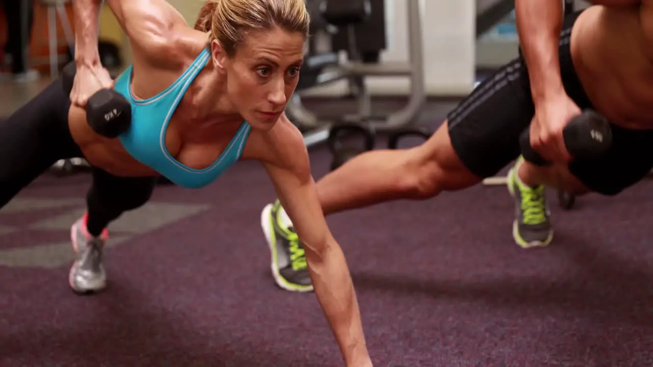 Two fit people lifting dumbbells in plank position