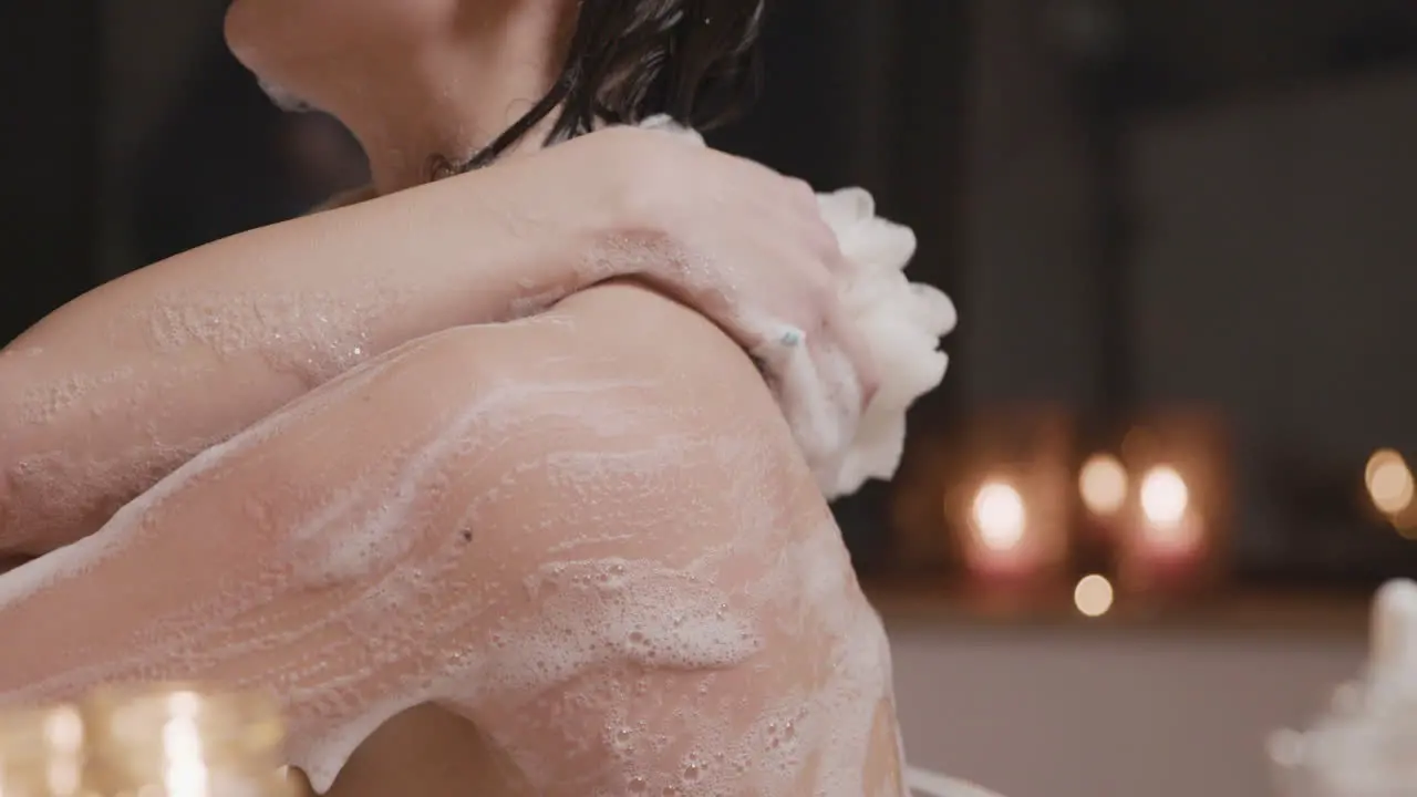 Side View Of A Woman Taking A Bath While Rubbing Her Back And Arms With Soap