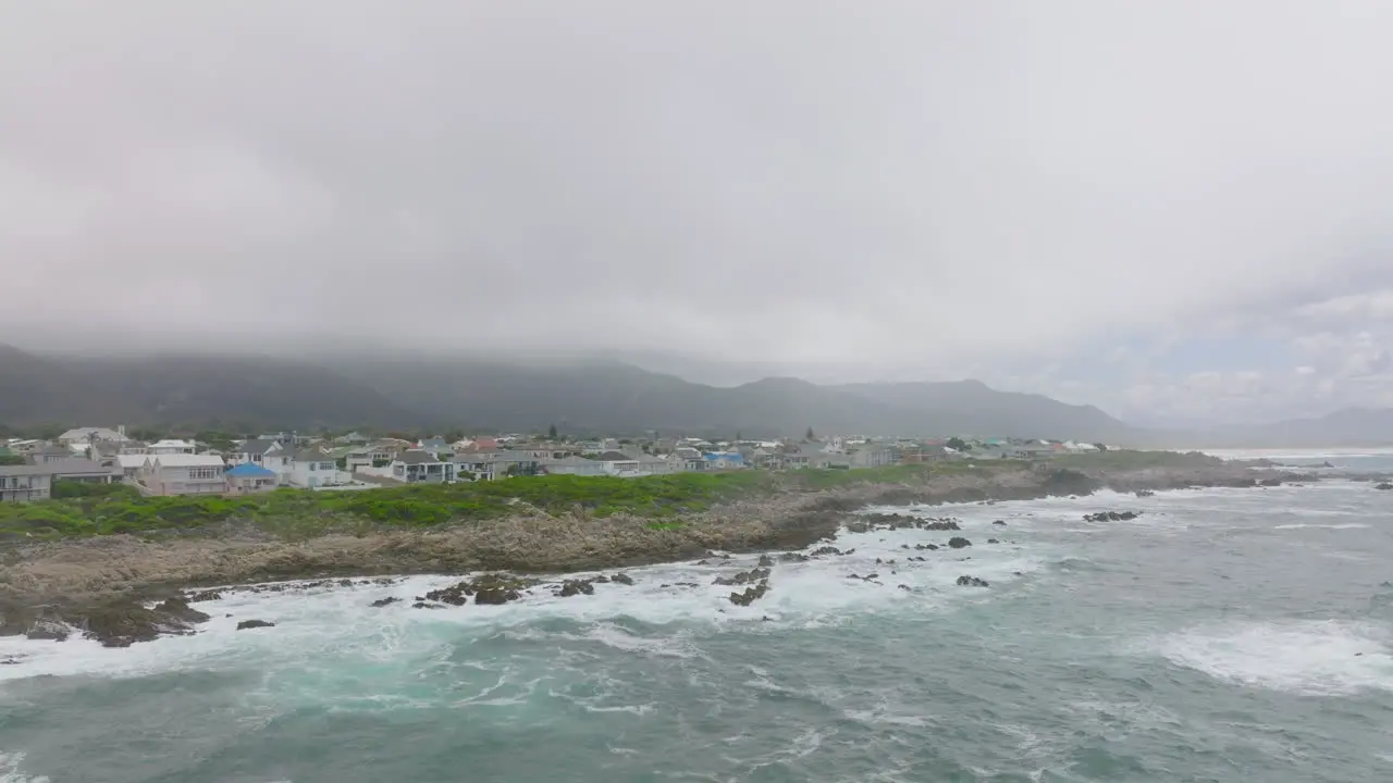 Slide and pan shot of waves crashing on rocks at sea coast Family houses in town in background