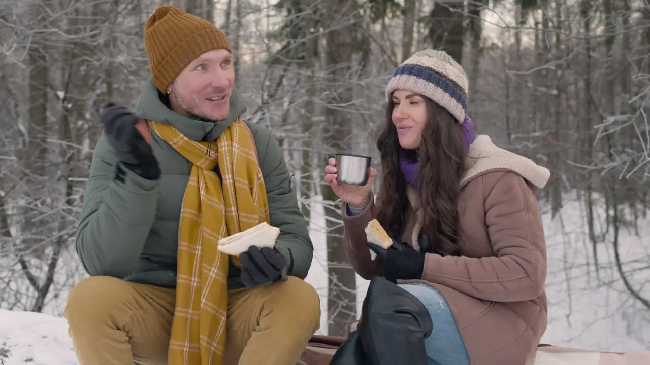 Husband And Wife In Winter Clothes Eating Sandwiches And Drinking Tea