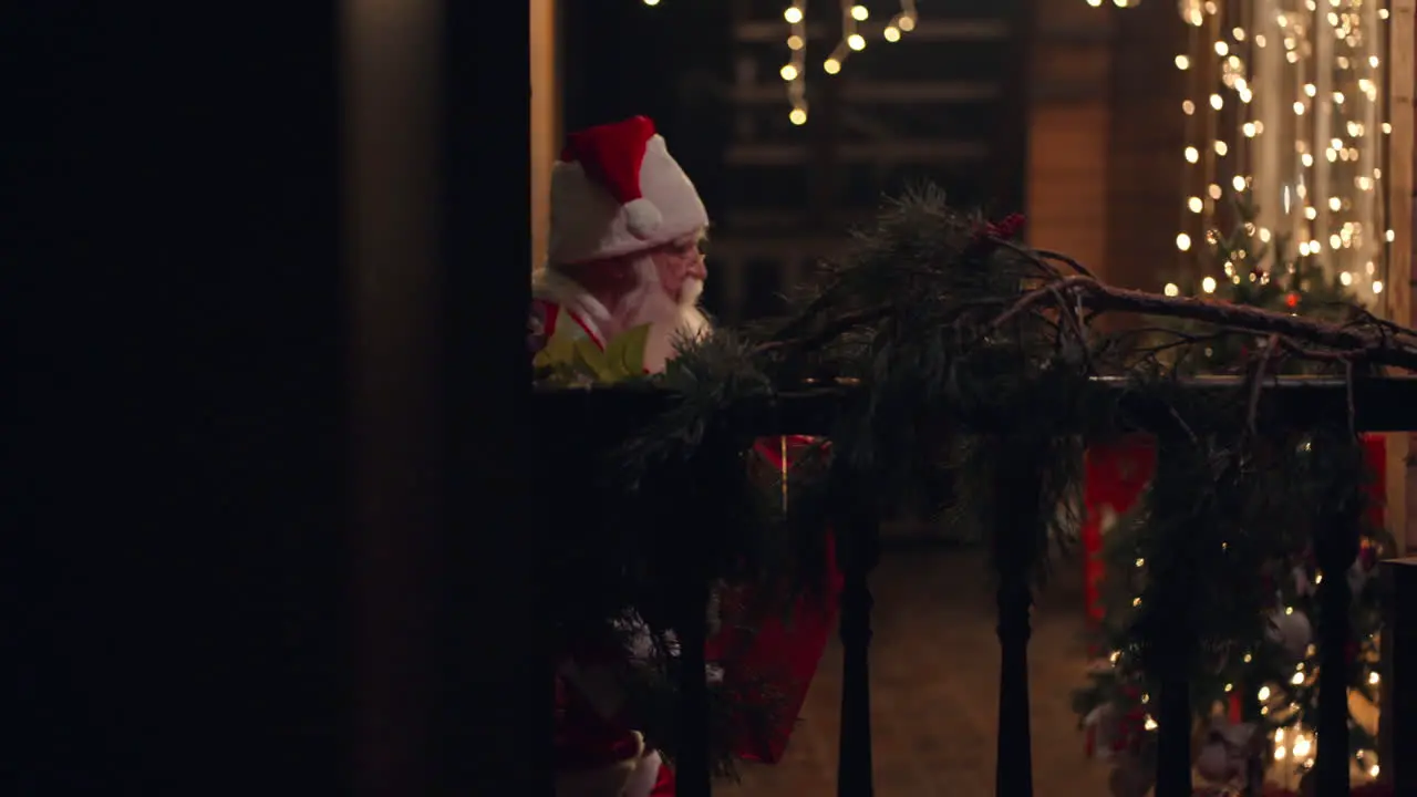 Side view Santa Claus is carrying a gift in his hands in winter on the street and comes to the door and enters the house with garlands and Christmas decorations