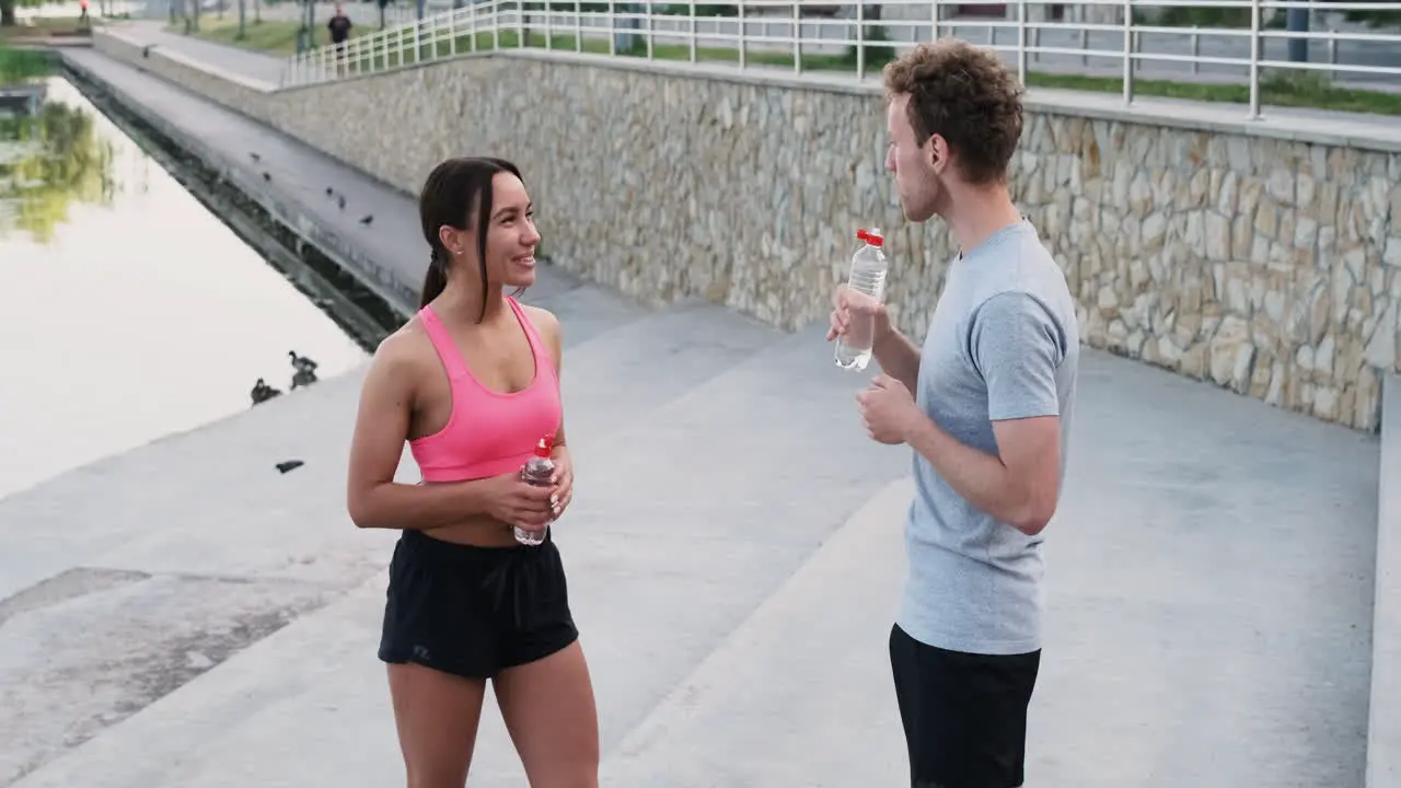 Happy Sportive Couple Drinking Water And Talking To Each Other While Taking A Break During Their Running Session In The City 1