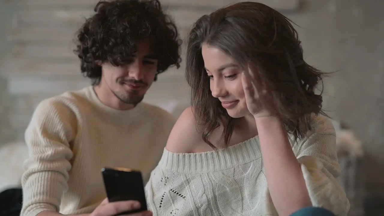 Linda Pareja Joven Sentada En La Cama Mirando Un Teléfono Y Usando Ropa De Invierno