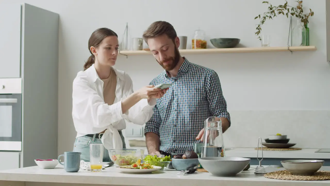 Mujer Tomando Fotos De Comida En La Mesa En Casa Mientras El Hombre Mira Y Dice Algo Divertido