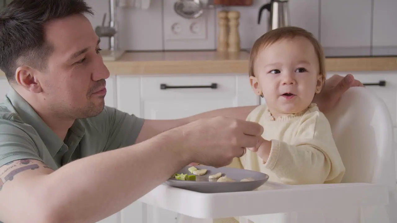 Padre Feliz Alimentando A Su Linda Niña Sentada En Su Silla Alta En La Cocina