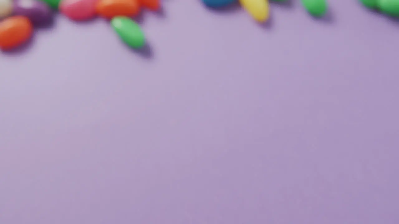 Video of close up of multi coloured sweets with copy space over purple background