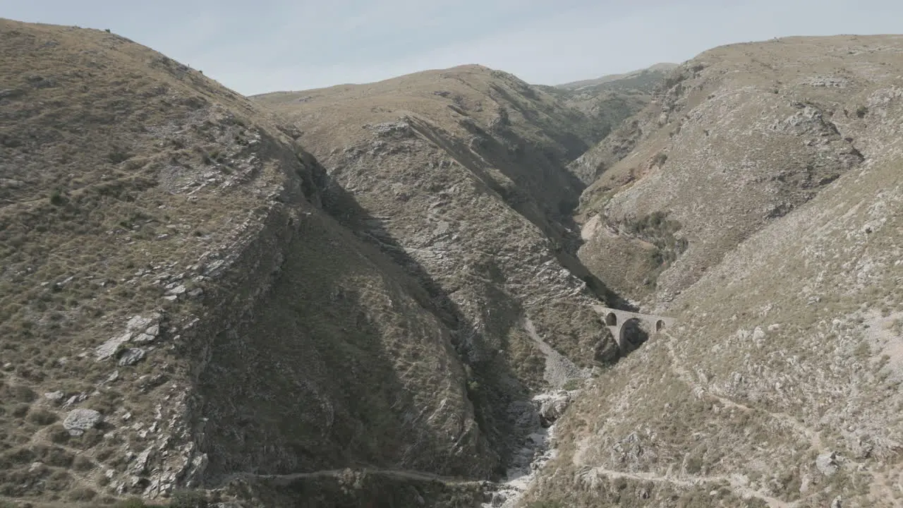 Drone shot of the Ali Pasha Bridge Outside of Gjirokaster Albania on a sunny day sitting in between the rocky mountains with a dry river LOG