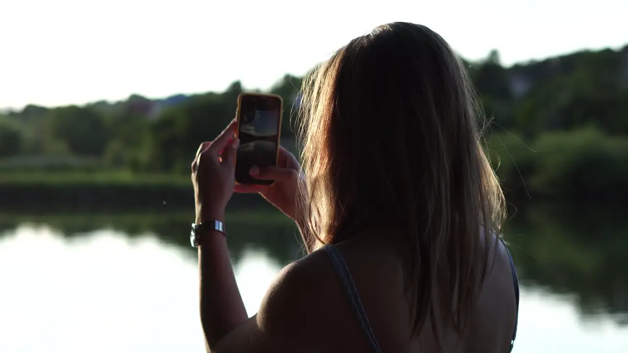 Backside shot of a girl taking photo of summer lake landscape