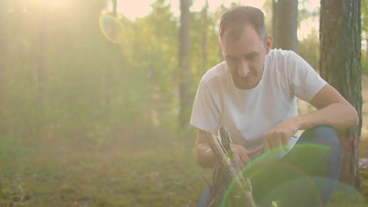 a man in the woods collects and sets up campfire sticks at sunset during a family camping trip