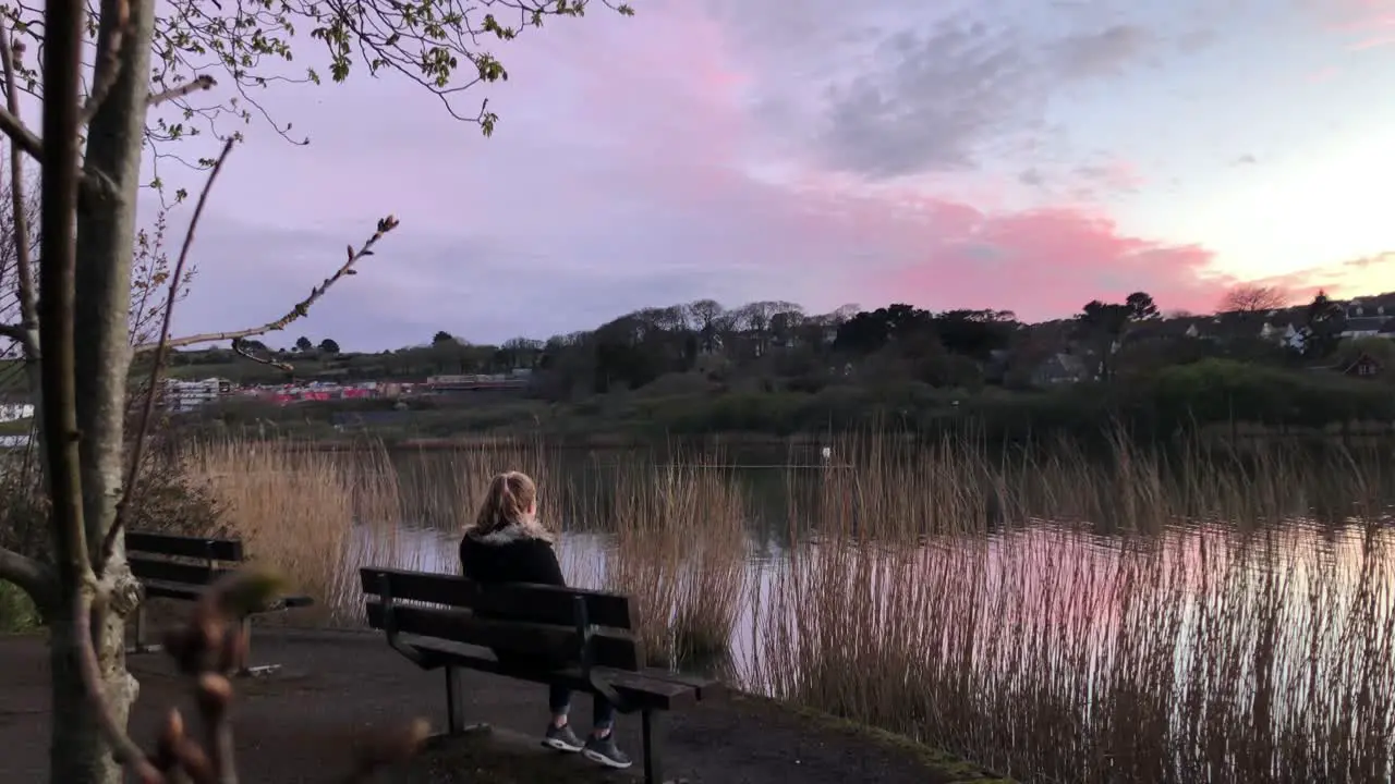 Lady Walks And Sits On The Bench On The Lake Shore To Watch Beautiful Sunset wide shot