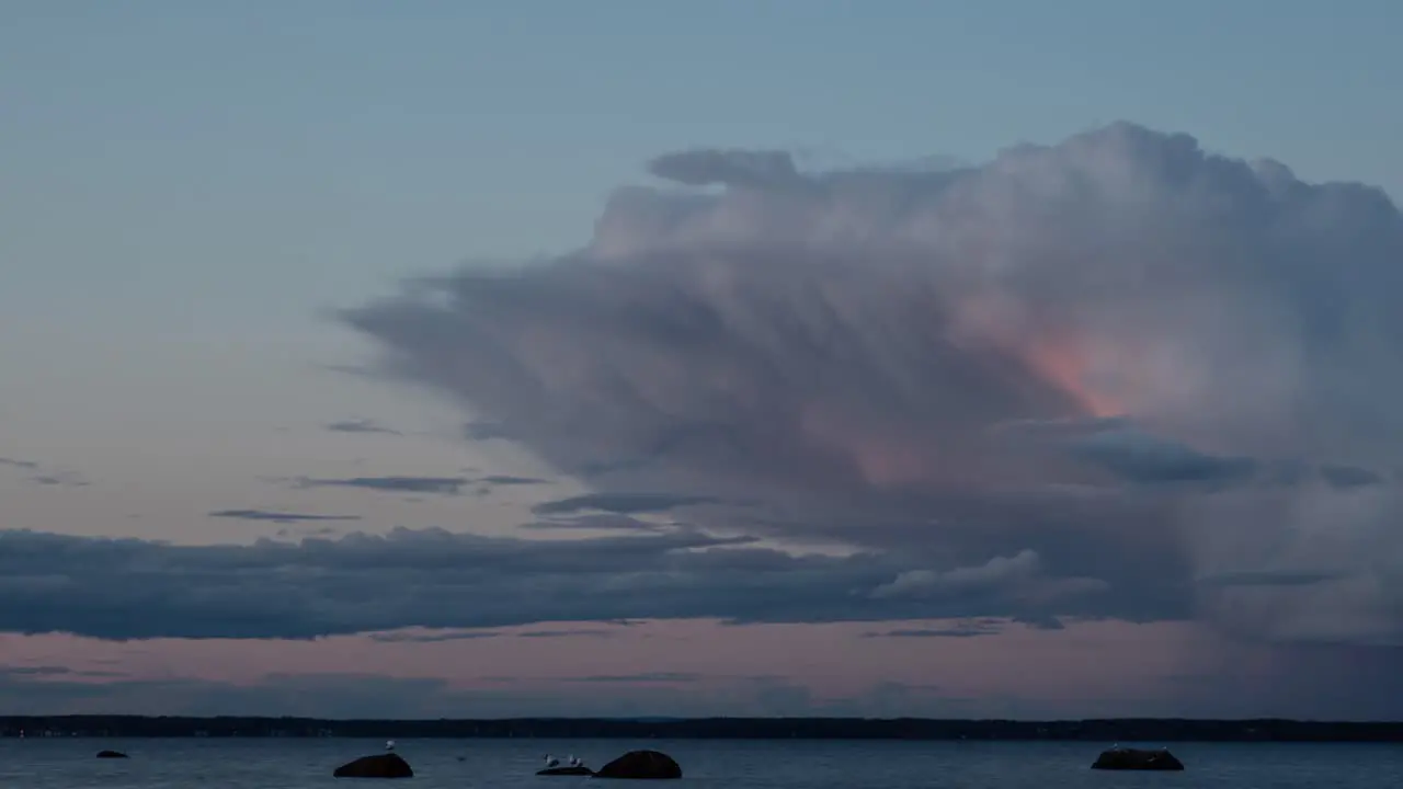 Time lapse video of color and form changing clouds over a fjord at sunset