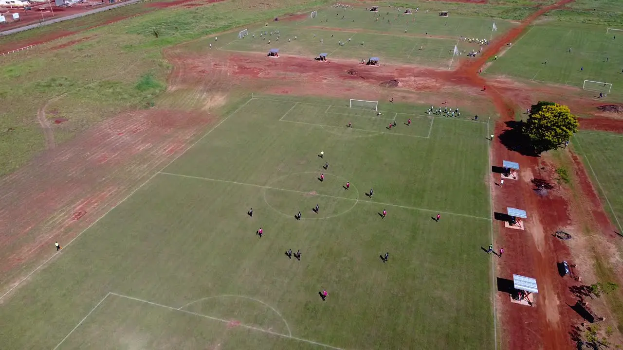 Drone high altitude approach on kids playing football match on pitch goal kick many other pitches in the background