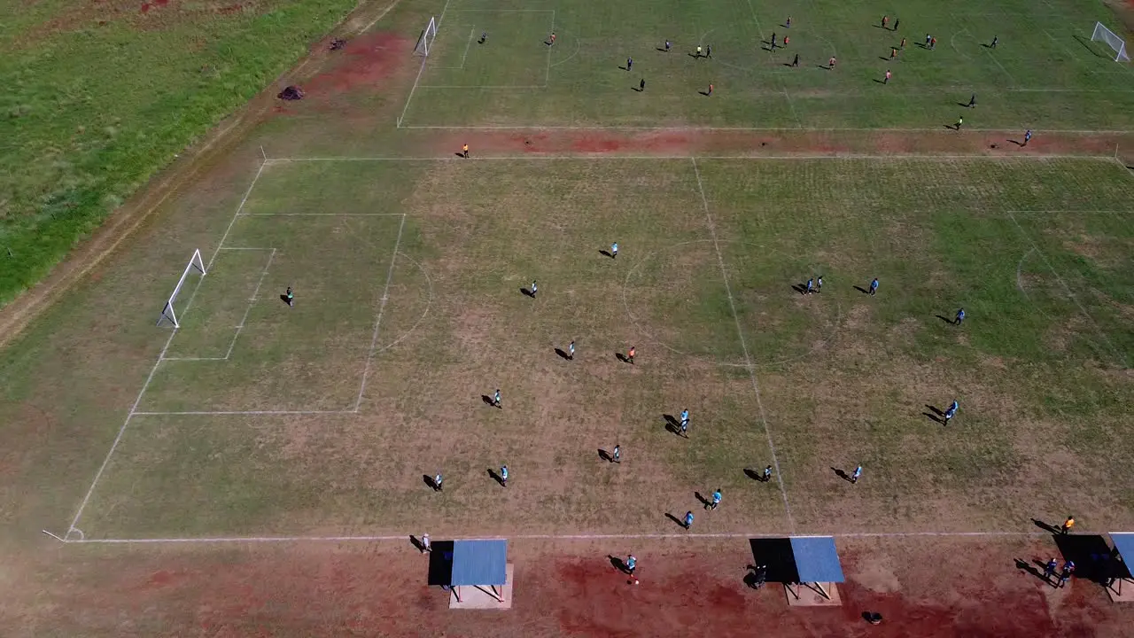 Drone high altitude strafe past kids playing football multiple football pitches at Posadas hipodrome