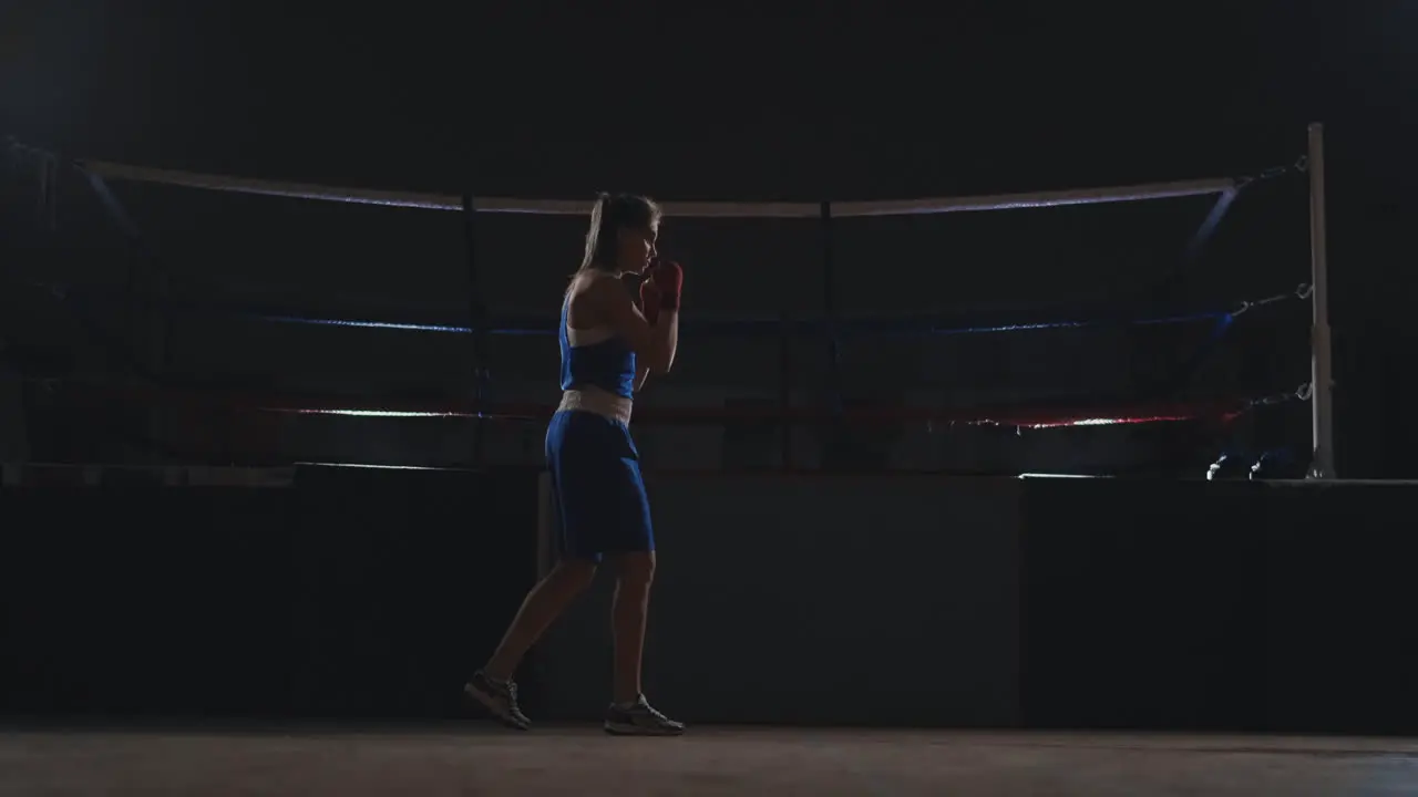 Professional beautiful female boxer otbryvatyvat blows conducting a fight with a shadow in a dark hall of the hall in slow motion in blue clothes and red bandages on her wrists flying around the object steadicam shot