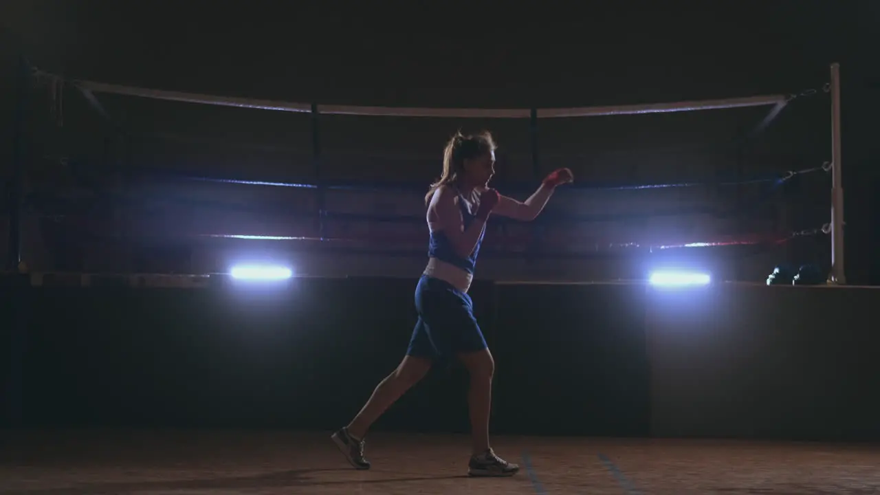 A beautiful woman conducts a shadow fight practicing technique and speed of strikes while training hard for future victories Dark gym background steadicam shot