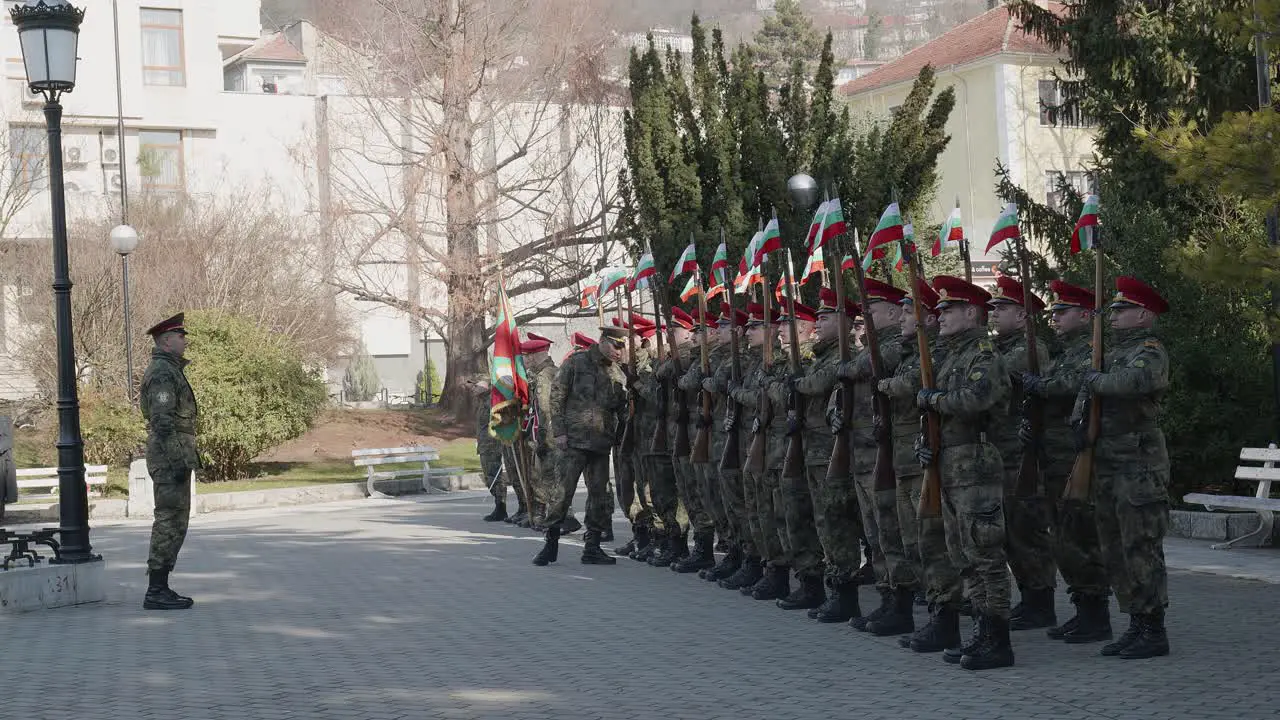 Ranks of soldiers presenting arms with national flags on memorial parade