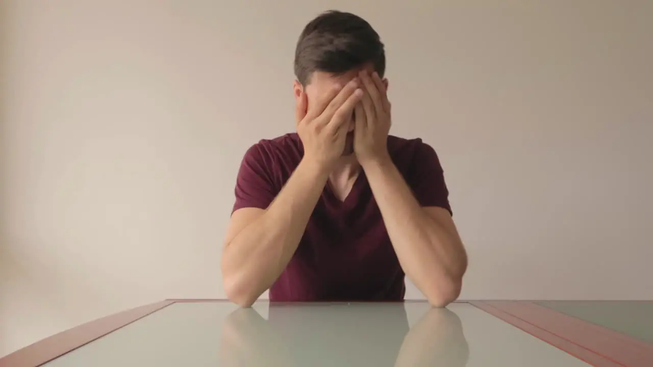 Young man sitting at table and stuggling to make a decisive choice medium close-up still shot indoors