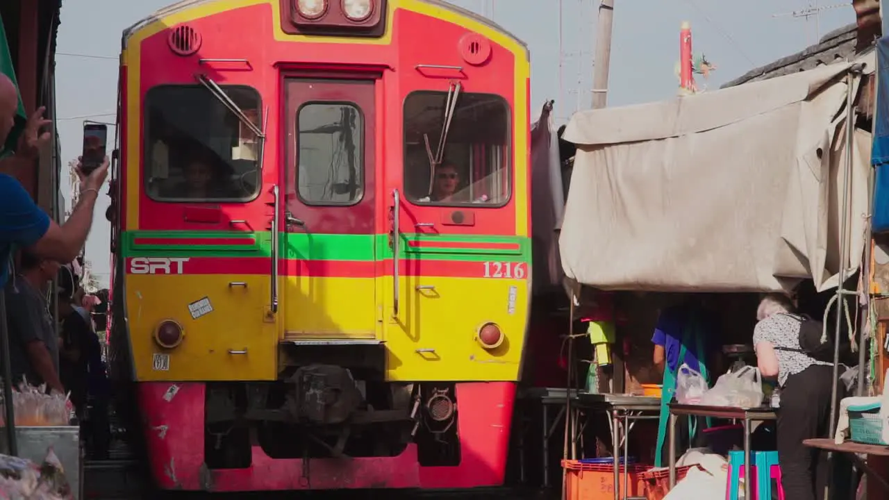 Establishing shot Elderly women tourist takes photo of the approaching train in Maeklong Samut Rail Road Market Thailand