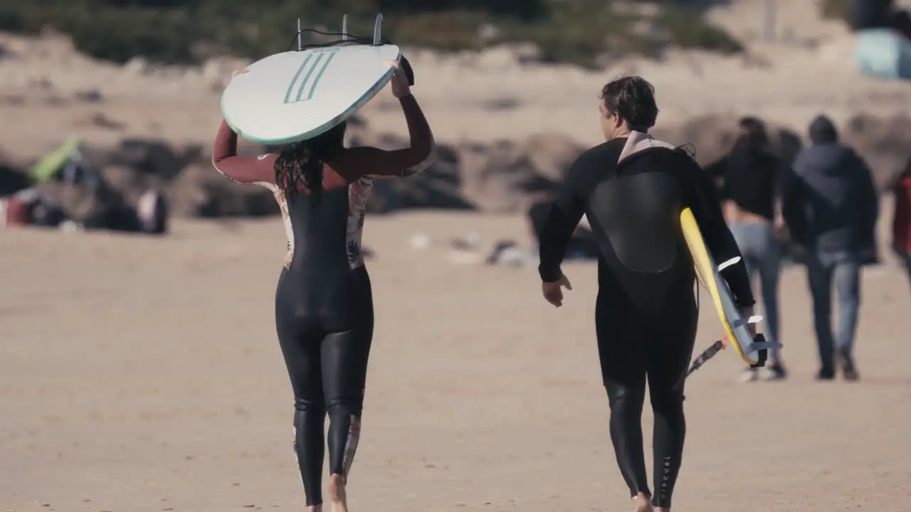 Two surfers carrying surfboards and walking away from sand beach back closeup view