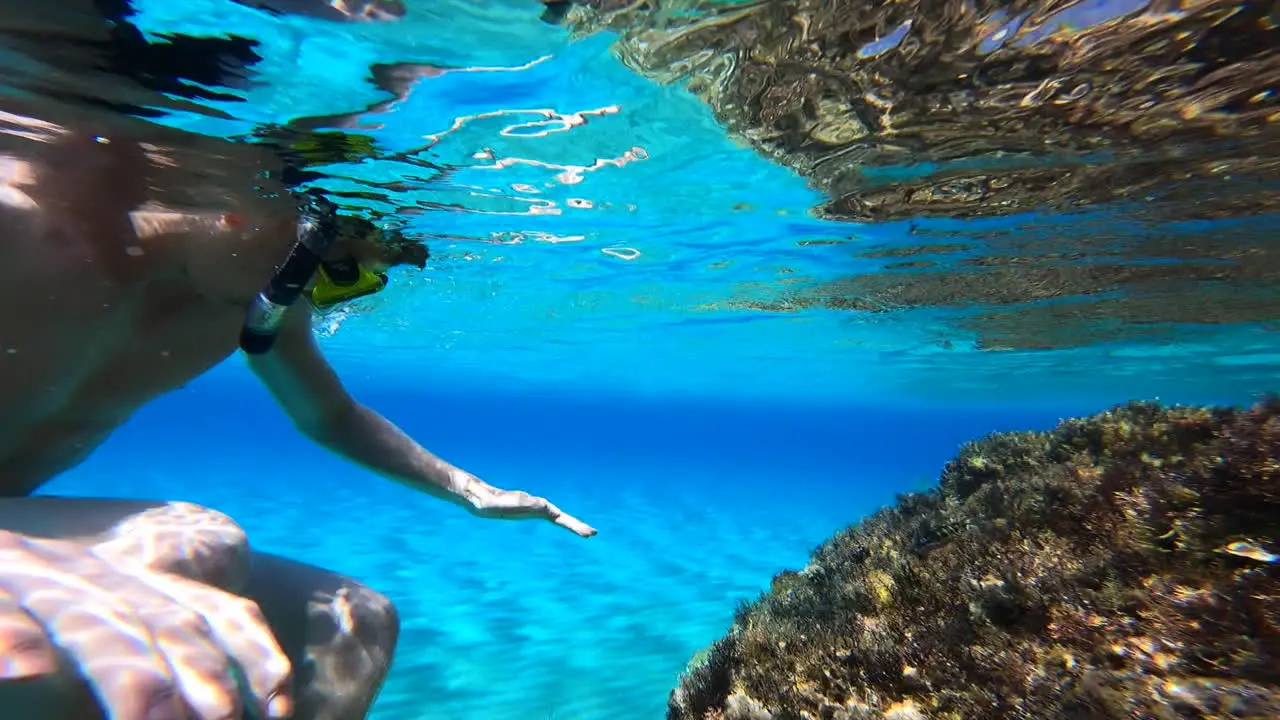 A young man looks underwater with a mask at a coral in greece while scuba diving