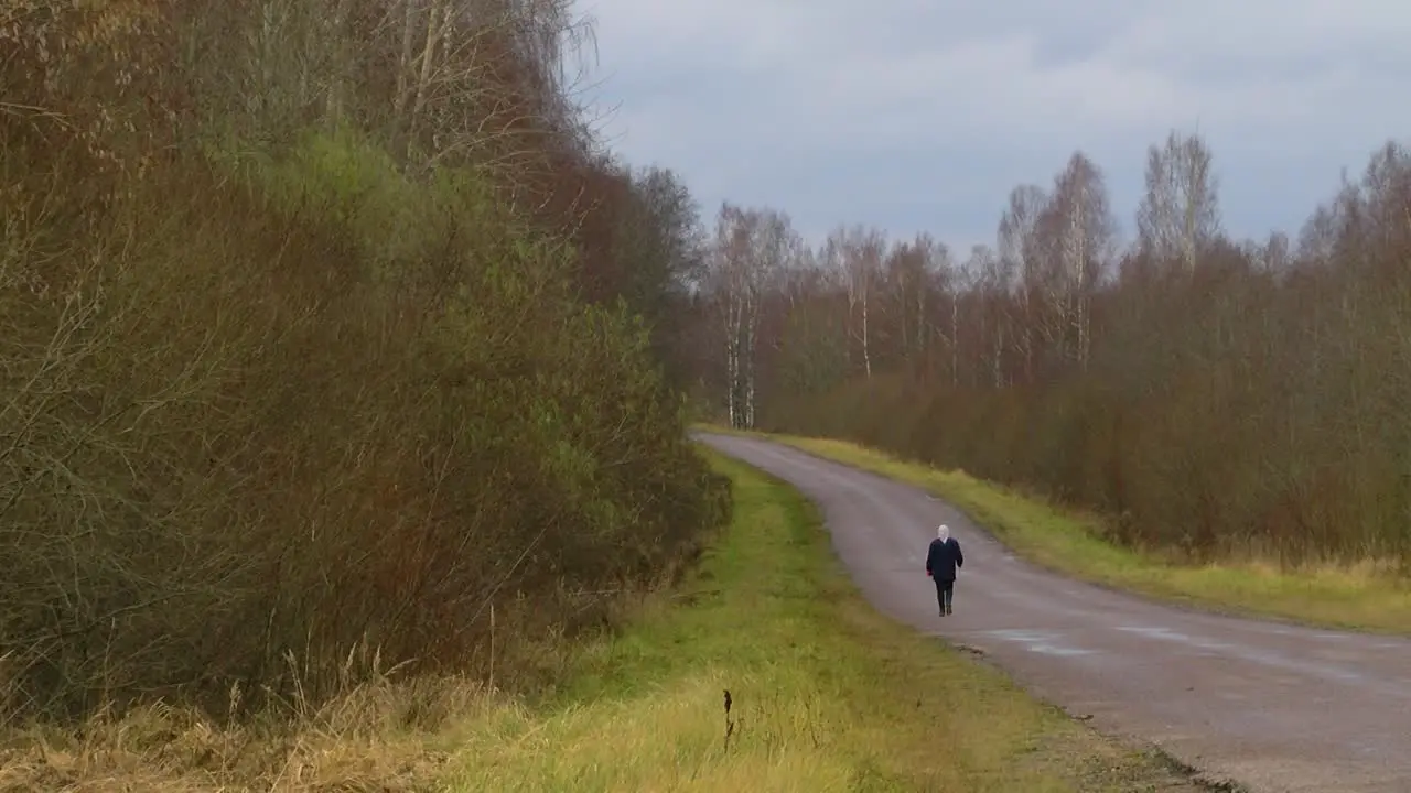 An old aunt goes alone with a crutch along an asphalt road