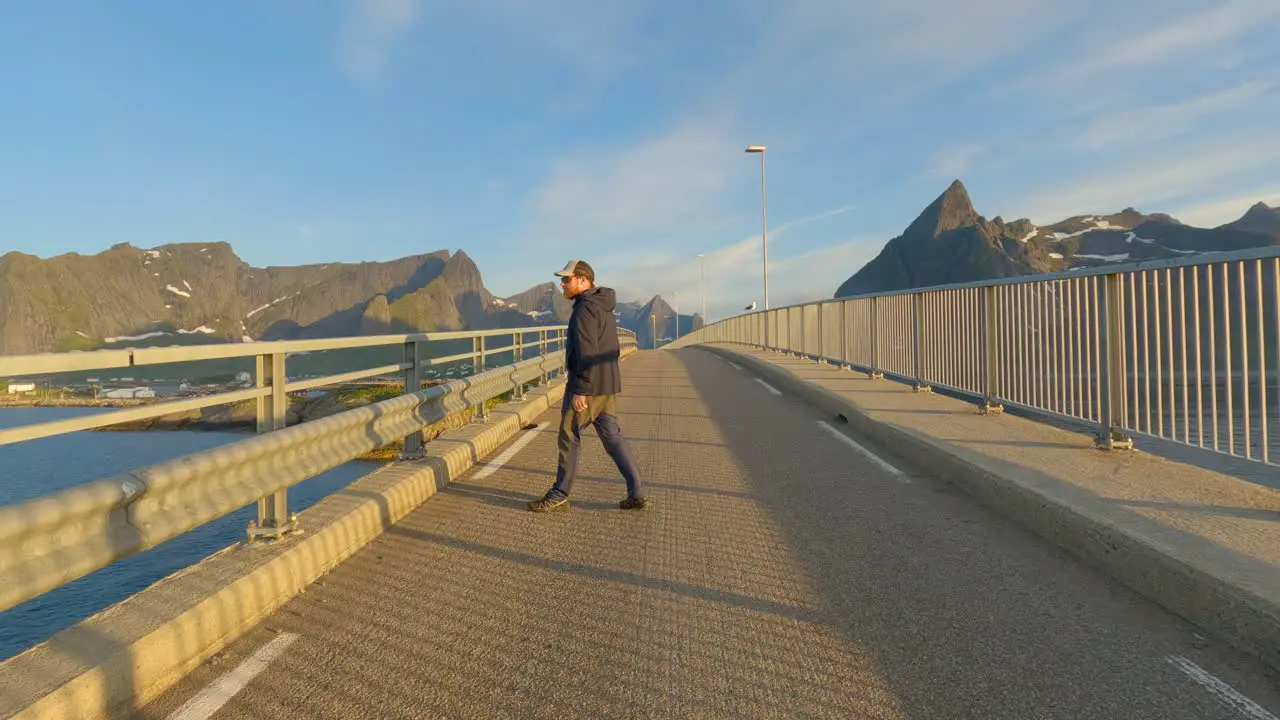 Young male enjoying the view during midnight sun on Hamnoy Bridge Lofoten Island Norway