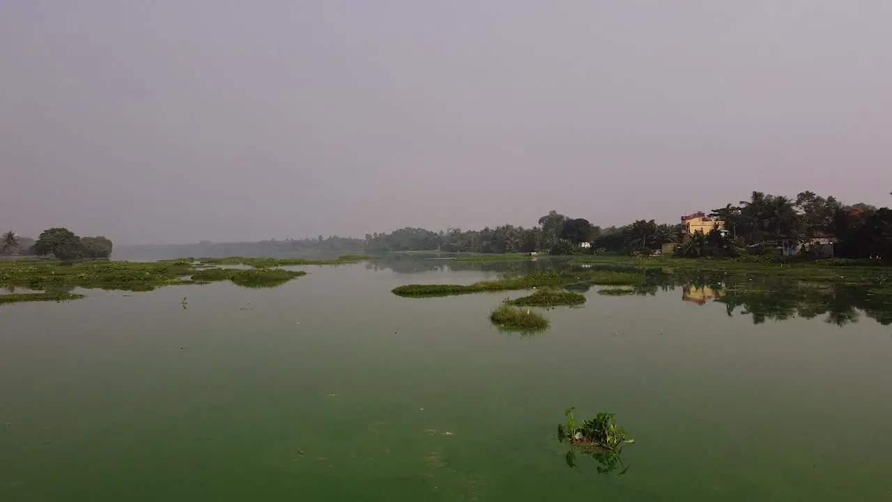 Aerial shot over small pond or lake in Indian village swan flying by