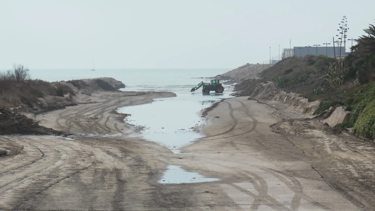 tractor moves sand near sea during overcast day