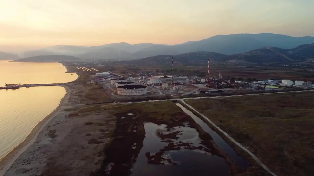 Aerial pan of oil refinery in a big valley by the sea at sunset