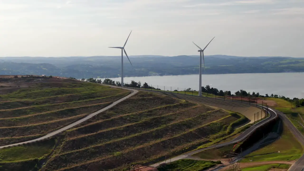 Aerial turn reveals landfill terraces on hillside high atop Susquehanna River wind turbines rotating on summer day