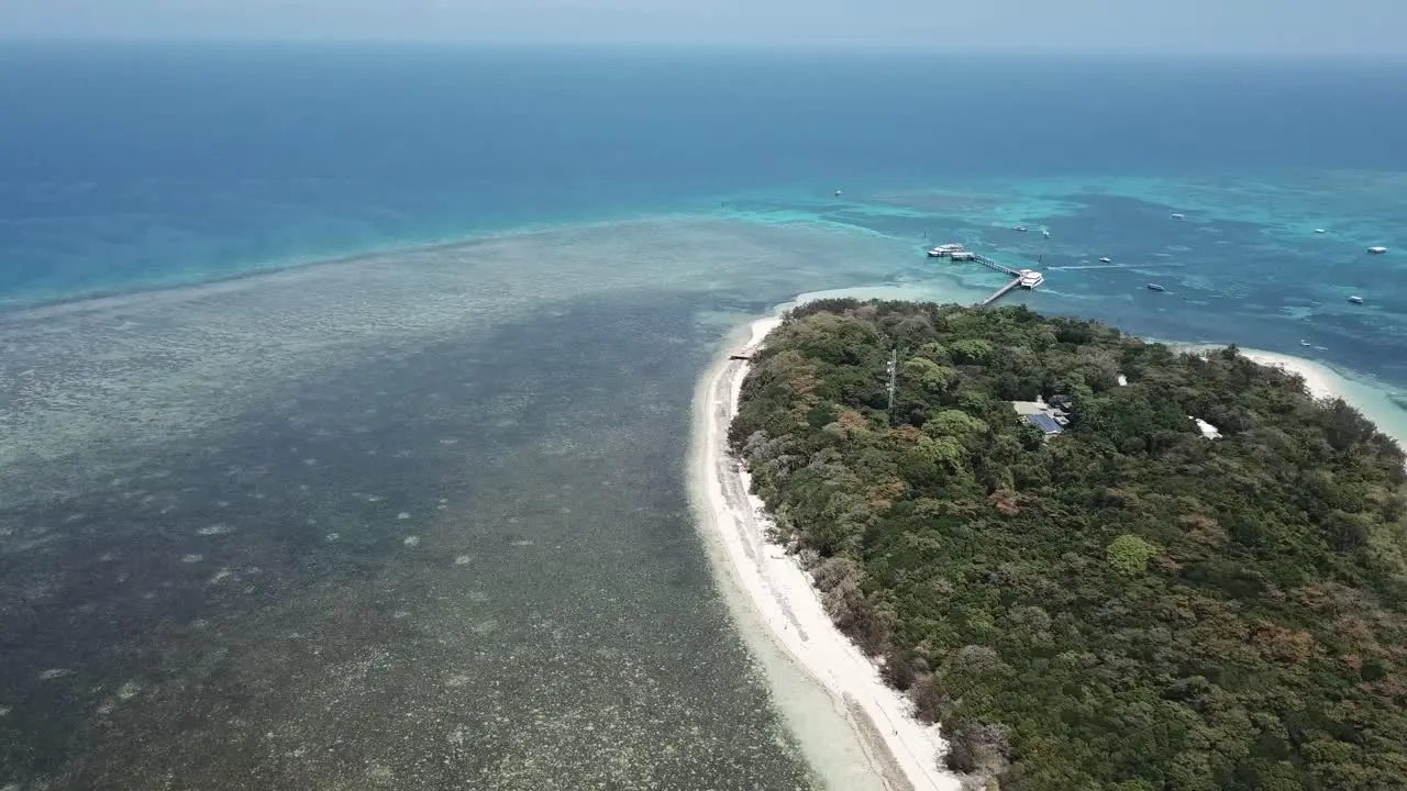 Drone aerial pan up onto the great barrier reef and tropical island with boats on the clear blue water