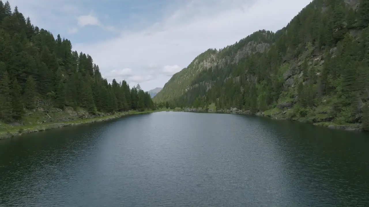 Ascending drone flight over mountain lake and green trees with waterfall Tilt down