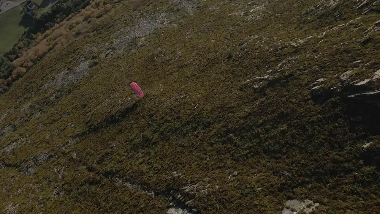 Aerial top down shot of paraglider flying over green mountains at sunny day in Norway