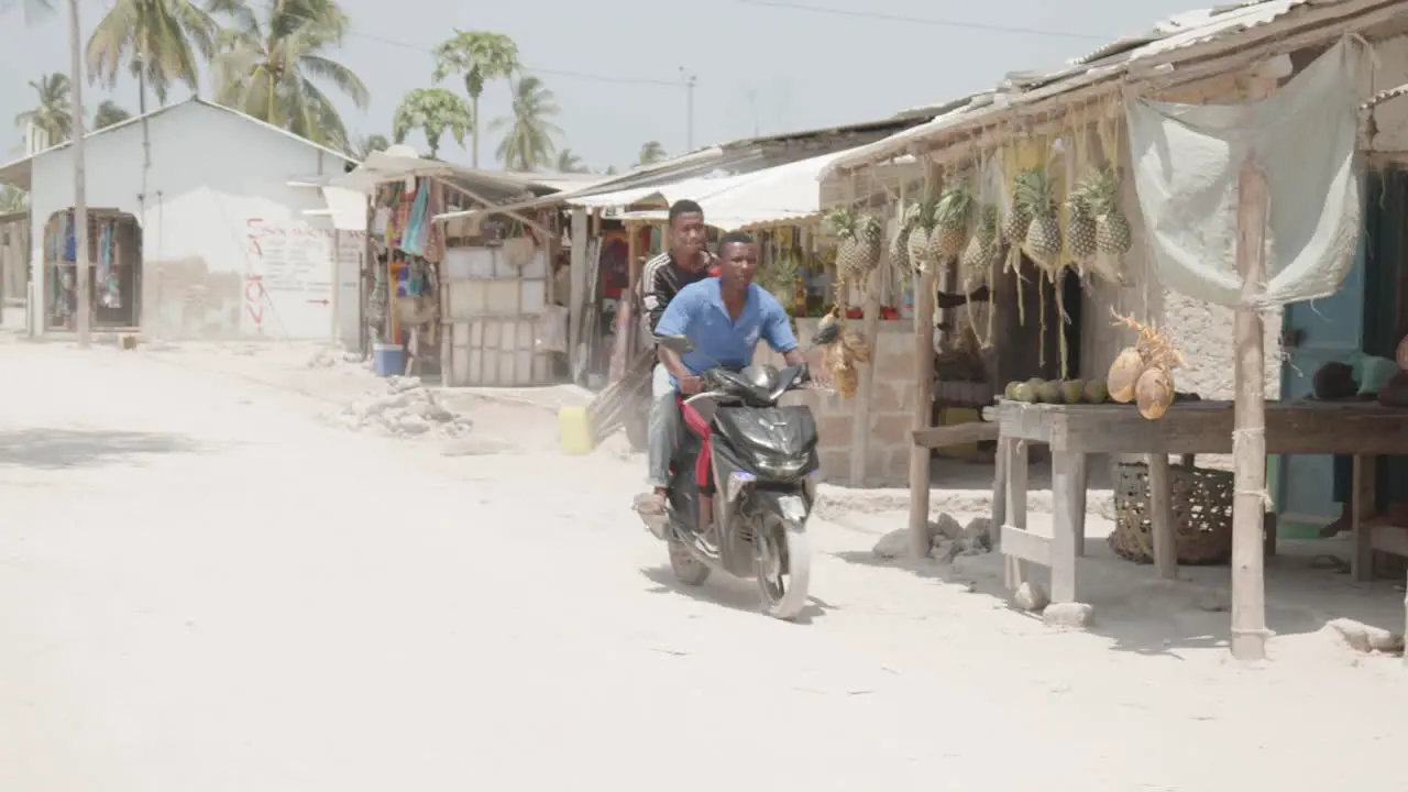 Two young black men driving on motorbike through village in Africa