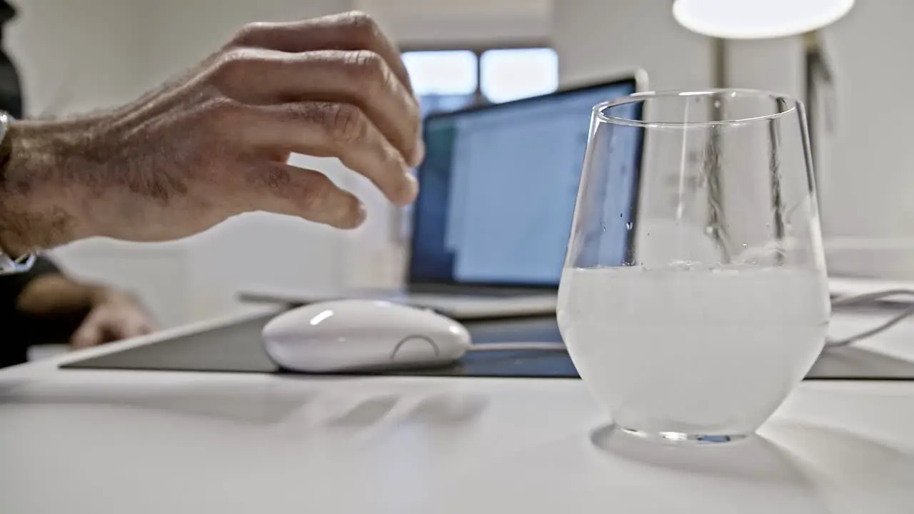 White person hand taking glass of water with effervescent tablet while working